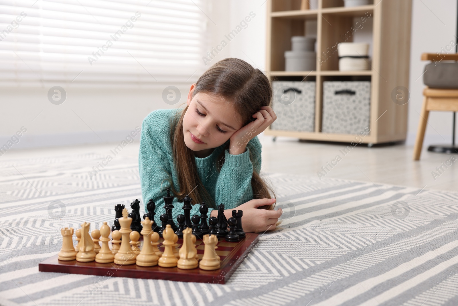 Photo of Cute girl playing chess on floor in room