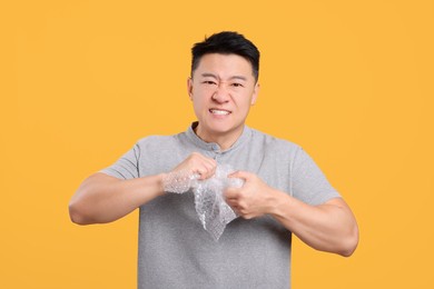 Photo of Emotional asian man with bubble wrap on orange background