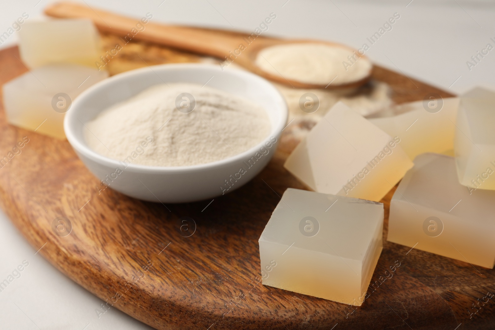 Photo of Agar-agar jelly cubes and bowl with powder on wooden board, closeup