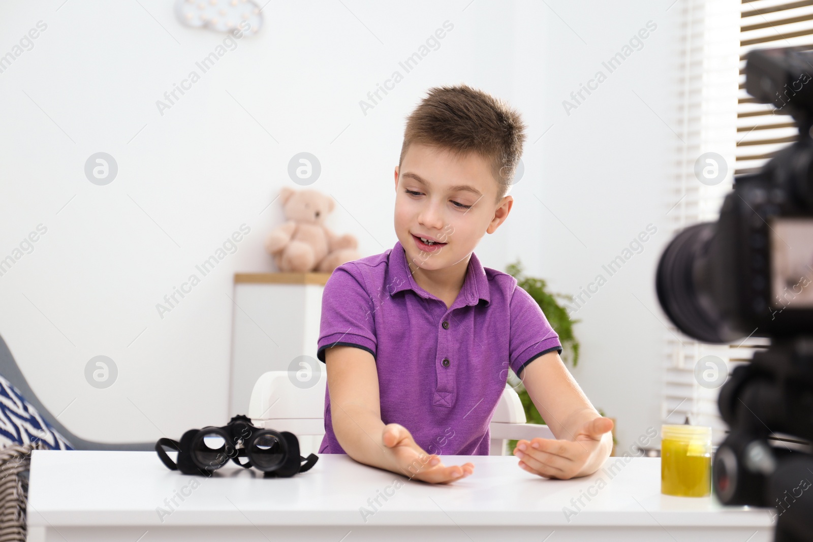 Photo of Cute little blogger with binoculars recording video at home