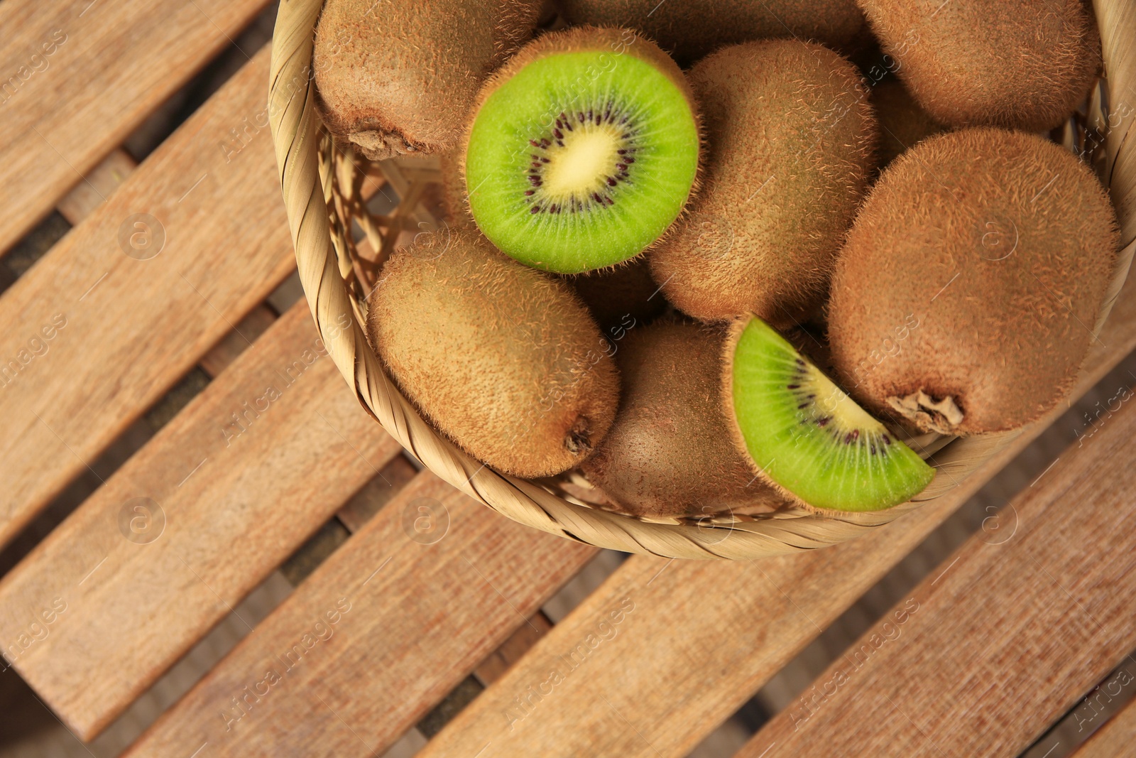 Photo of Wicker basket with whole and cut kiwis on wooden table, top view. Space for text