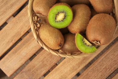 Wicker basket with whole and cut kiwis on wooden table, top view. Space for text