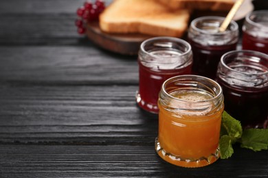 Photo of Jars of different jams on black wooden table, space for text