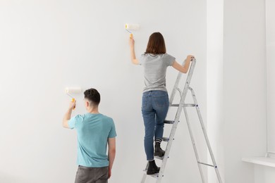 Photo of Young man and woman painting wall with rollers indoors. Room renovation