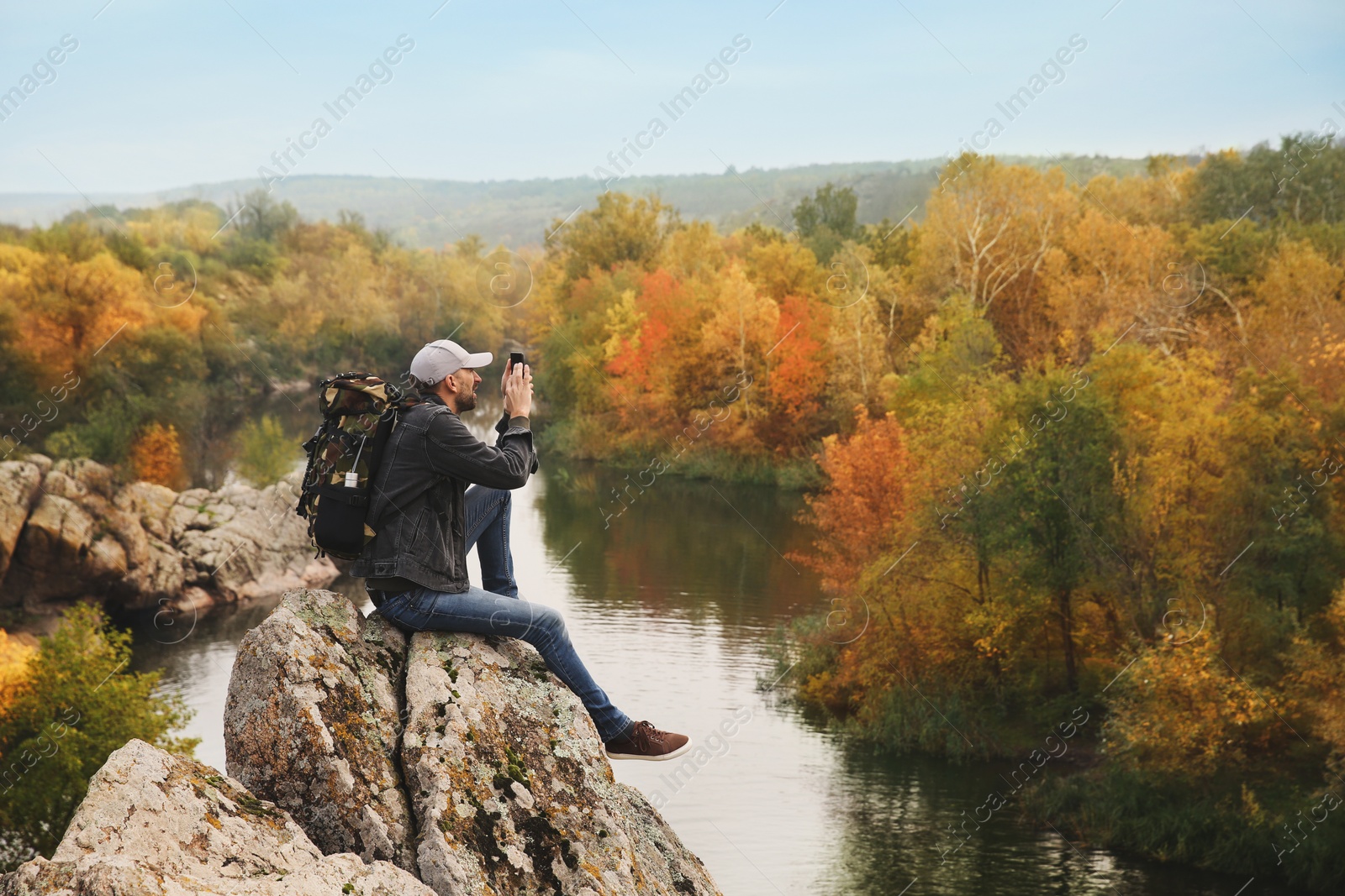 Photo of Hiker with smartphone sitting on steep cliff near mountain river