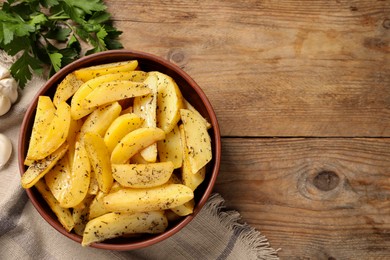 Photo of Bowl with tasty baked potato wedges and parsley on wooden table, flat lay. Space for text