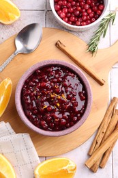 Tasty cranberry sauce in bowl and ingredients on white tiled table, flat lay