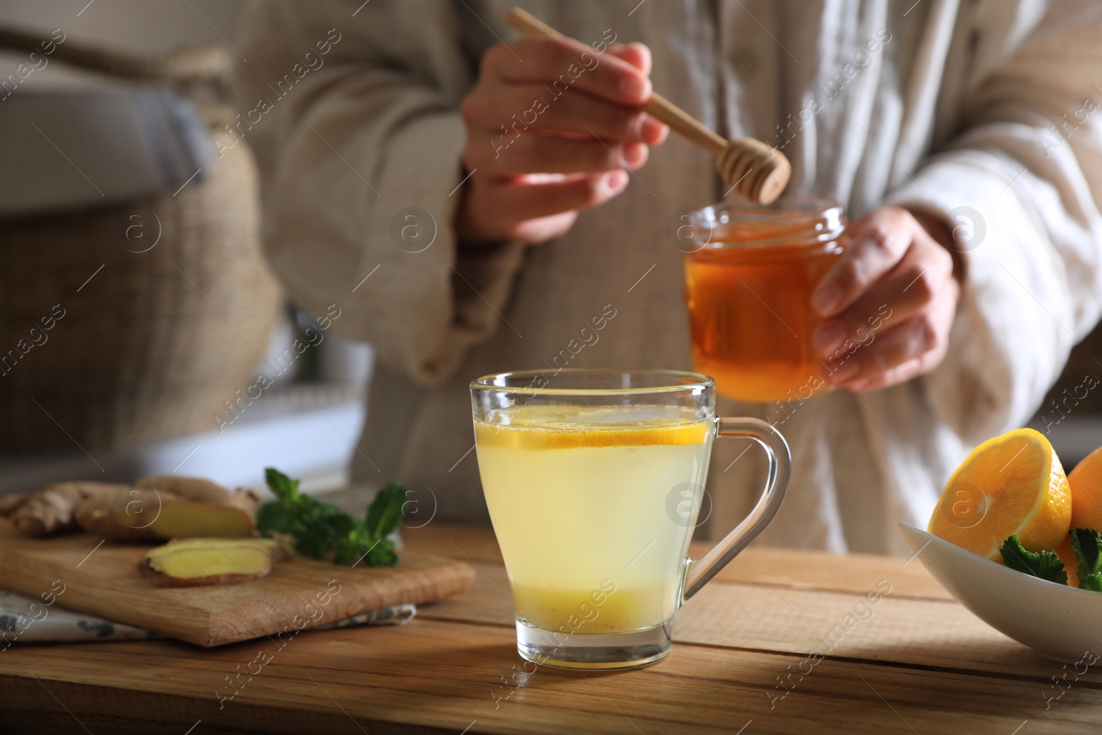 Photo of Woman making aromatic ginger tea at wooden table indoors, closeup