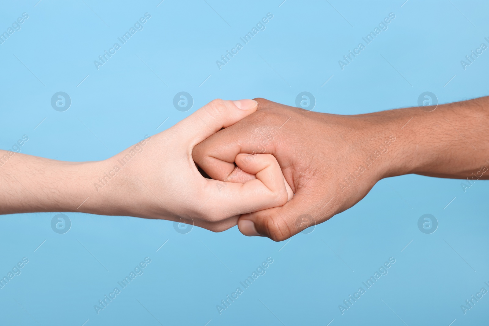 Photo of International relationships. People strongly joining hands on light blue background, closeup