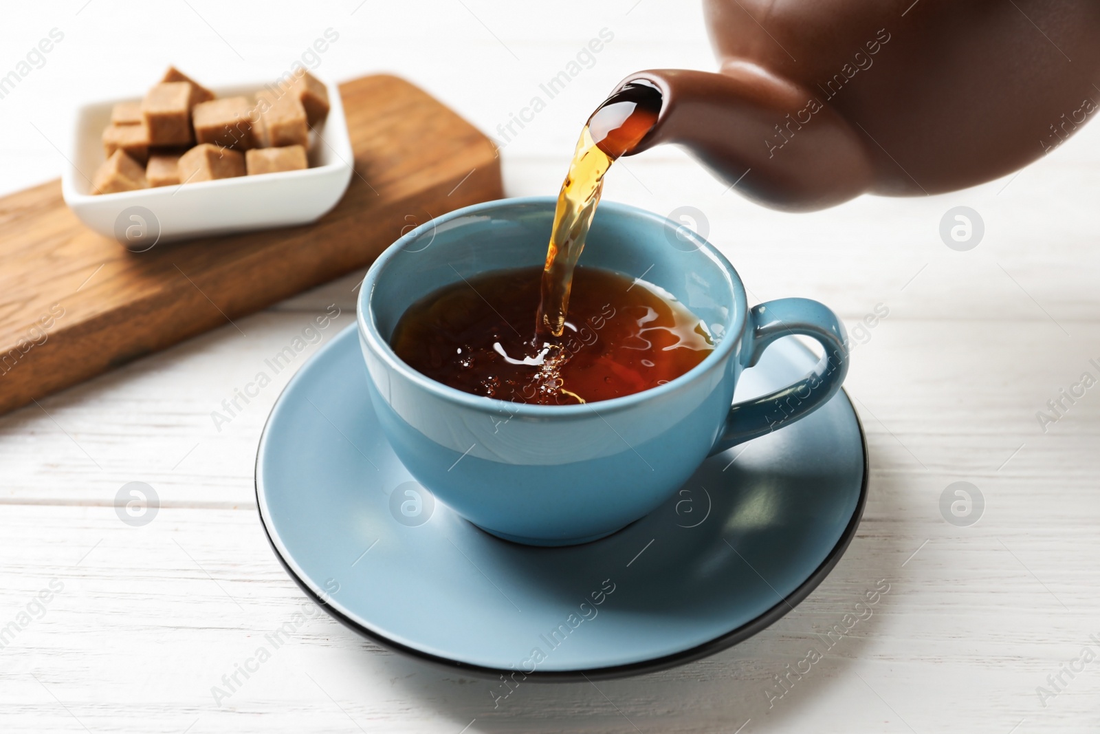 Photo of Pouring black tea into ceramic cup on wooden table