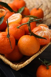 Photo of Fresh ripe tangerines with green leaves in wicker basket on table, closeup