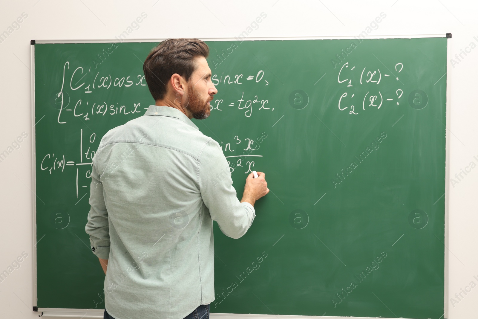 Photo of Mature teacher explaining mathematics at chalkboard in classroom