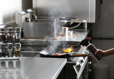 Photo of Female chef cooking meat with manual gas burner on stove in restaurant kitchen, closeup