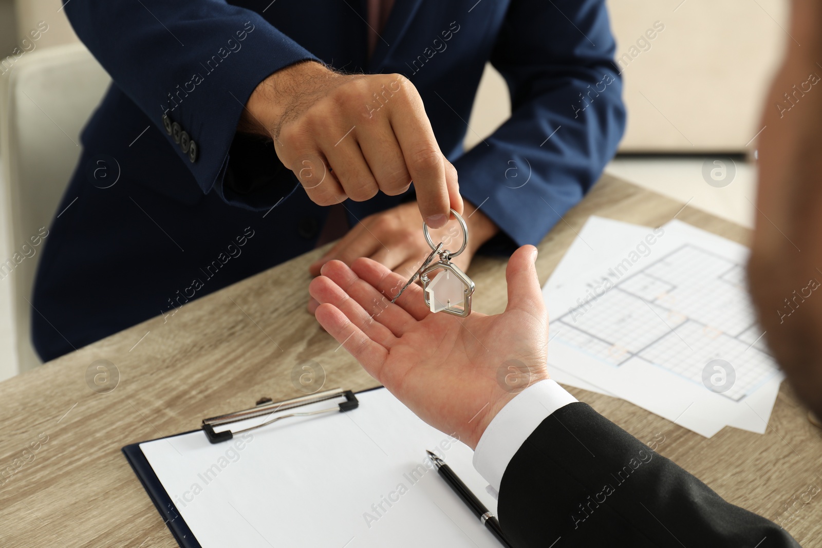 Photo of Real estate agent giving key to client at table in office, closeup