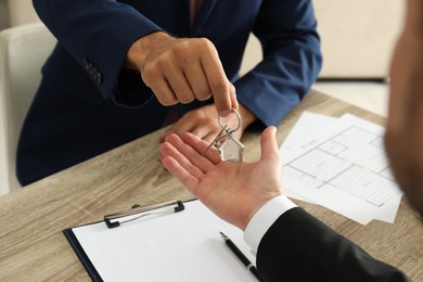 Photo of Real estate agent giving key to client at table in office, closeup