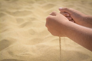 Photo of Child pouring sand from hands on beach, closeup with space for text. Fleeting time concept