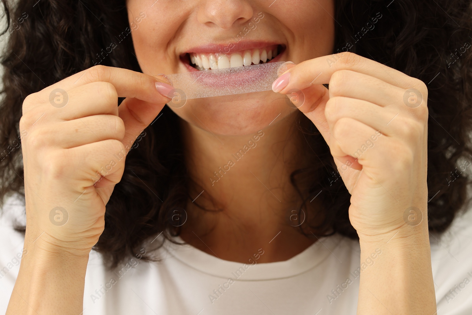 Photo of Young woman applying whitening strip on her teeth, closeup