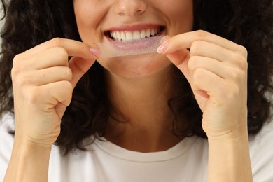 Photo of Young woman applying whitening strip on her teeth, closeup