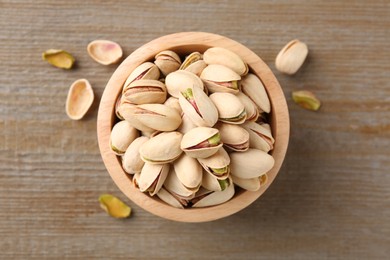 Tasty pistachios in bowl on wooden table, top view