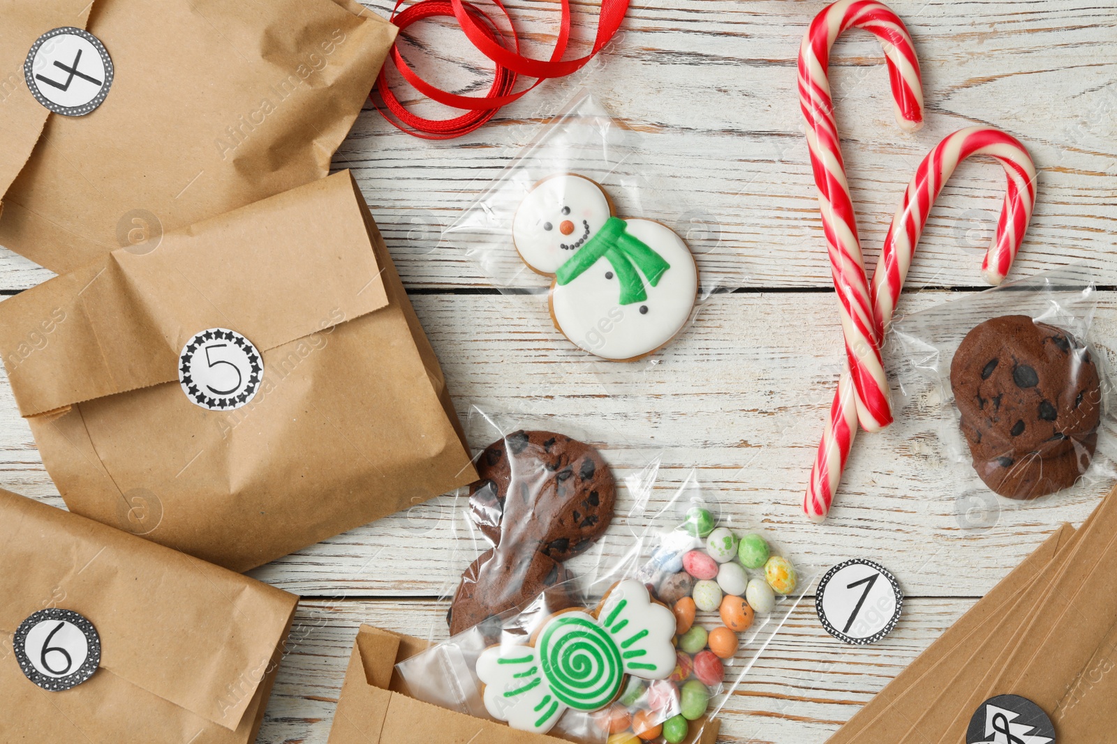 Photo of Flat lay composition with gift bags and Christmas treats on white wooden table. Creating advent calendar