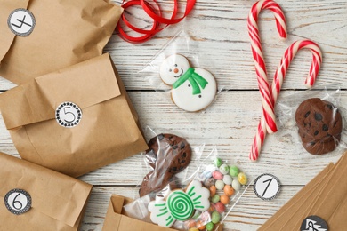 Photo of Flat lay composition with gift bags and Christmas treats on white wooden table. Creating advent calendar