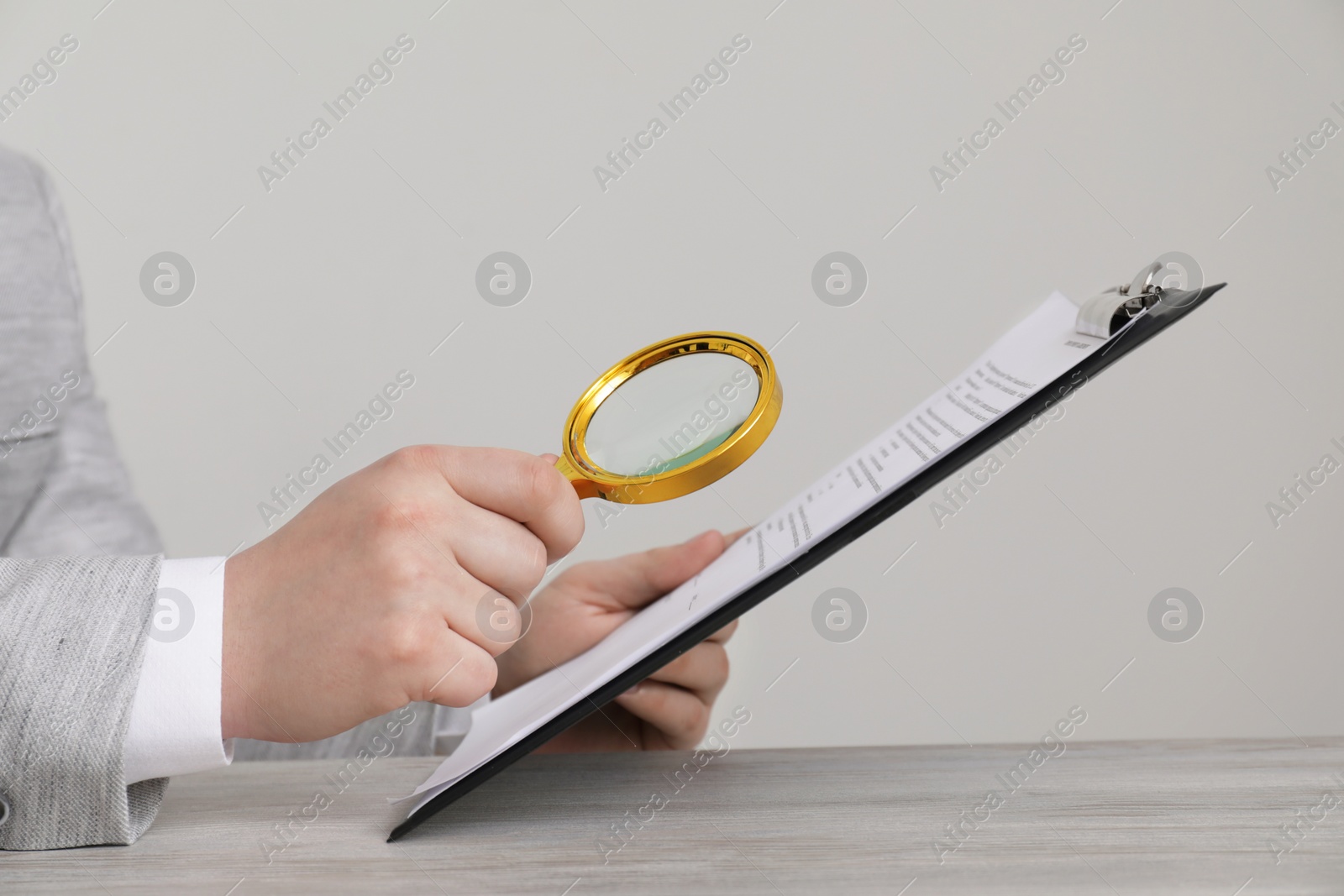 Photo of Man looking at document through magnifier at white wooden table, closeup. Searching concept