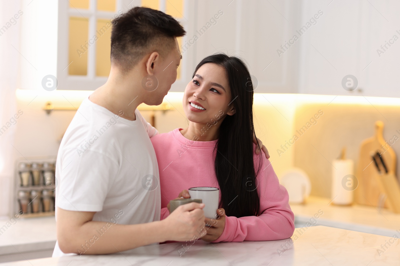 Photo of Lovely couple with cups of drink enjoying time together in kitchen, space for text