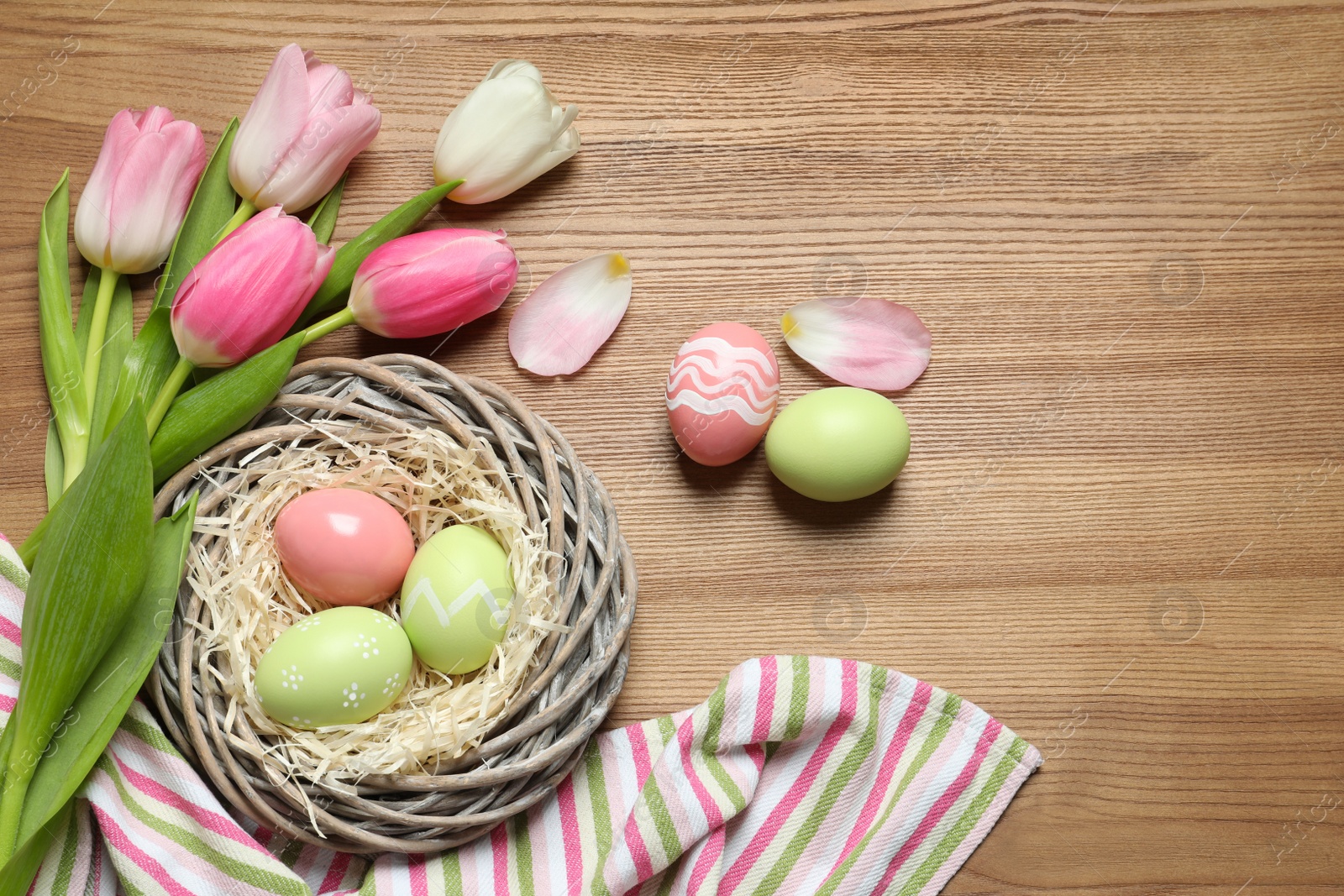 Photo of Flat lay composition with painted Easter eggs and tulips on wooden table, space for text