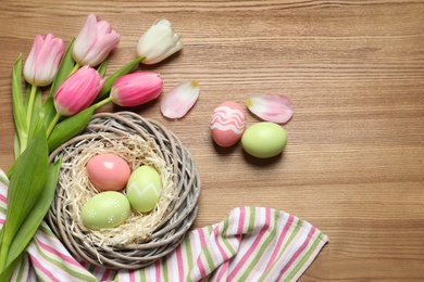 Flat lay composition with painted Easter eggs and tulips on wooden table, space for text