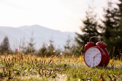 Red alarm clock on grass outdoors in morning, space for text