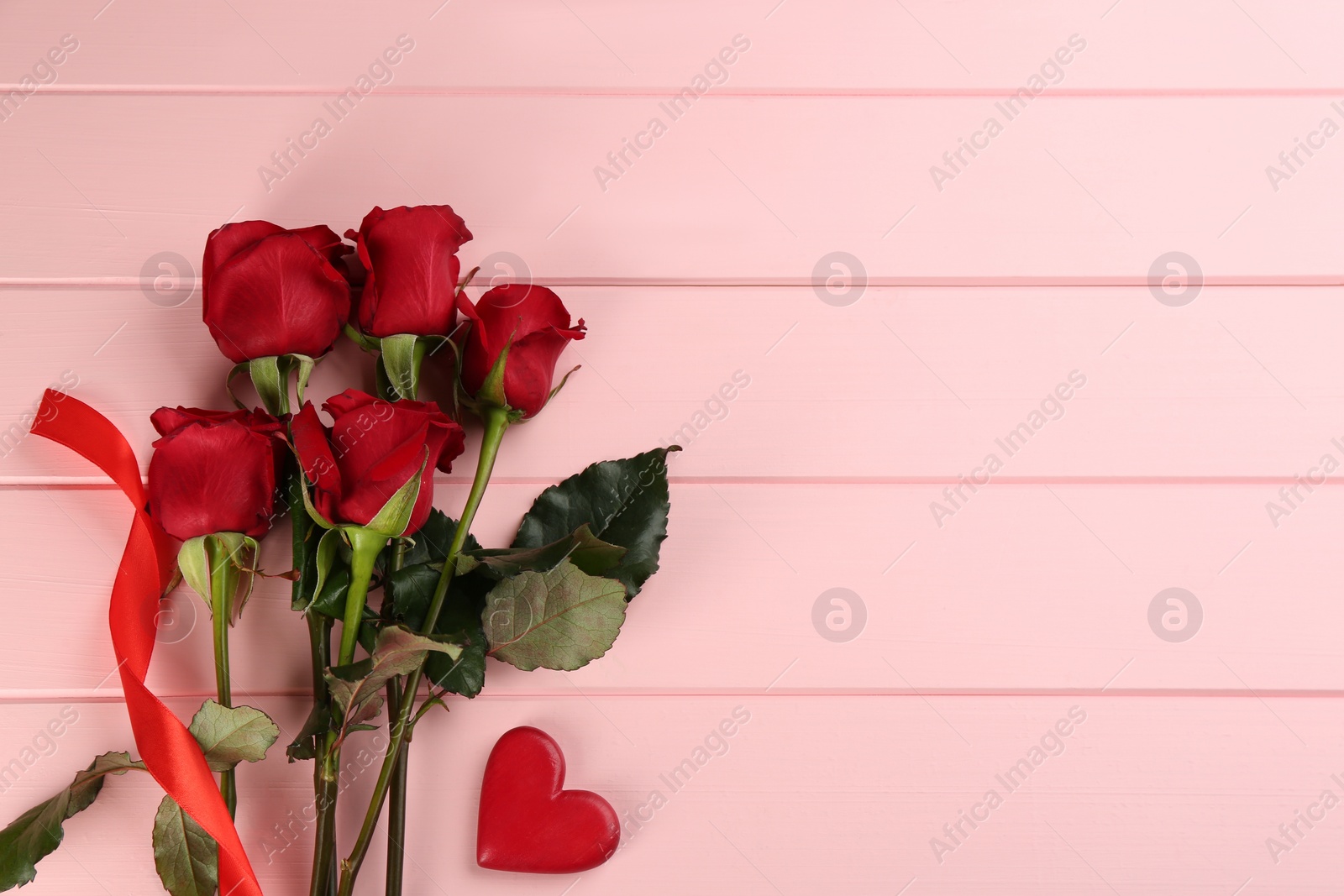Photo of Beautiful red roses and decorative heart on pink wooden background, flat lay with space for text. Valentine's Day celebration
