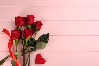 Beautiful red roses and decorative heart on pink wooden background, flat lay with space for text. Valentine's Day celebration