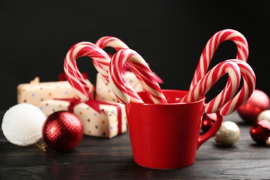 Photo of Many sweet candy canes in cup, gift boxes and Christmas decor on wooden table