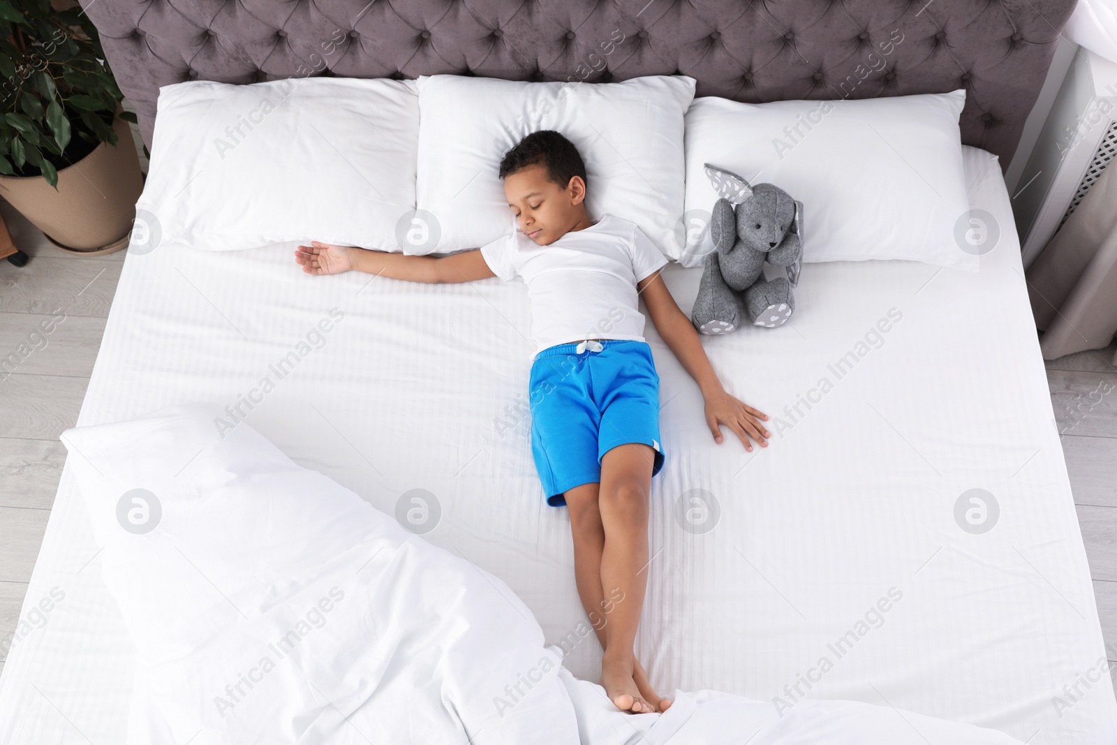 Photo of Cute little African-American boy with toy rabbit sleeping in bed, top view