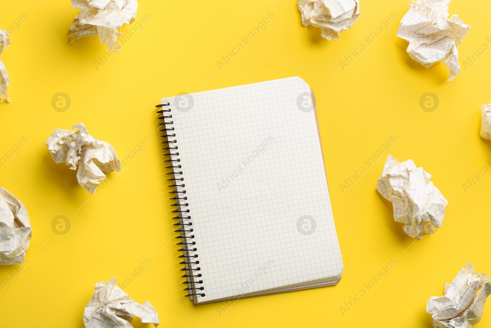 Photo of Notebook and crumpled sheets of paper on yellow background, flat lay. Space for text