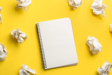 Notebook and crumpled sheets of paper on yellow background, flat lay. Space for text