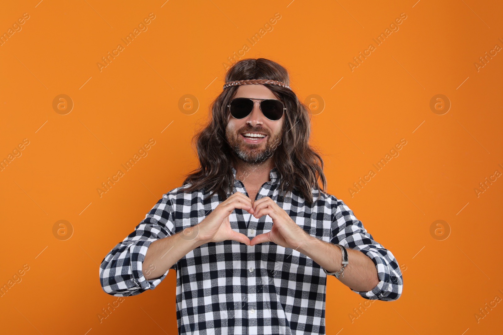 Photo of Hippie man in sunglasses making heart with hands on orange background