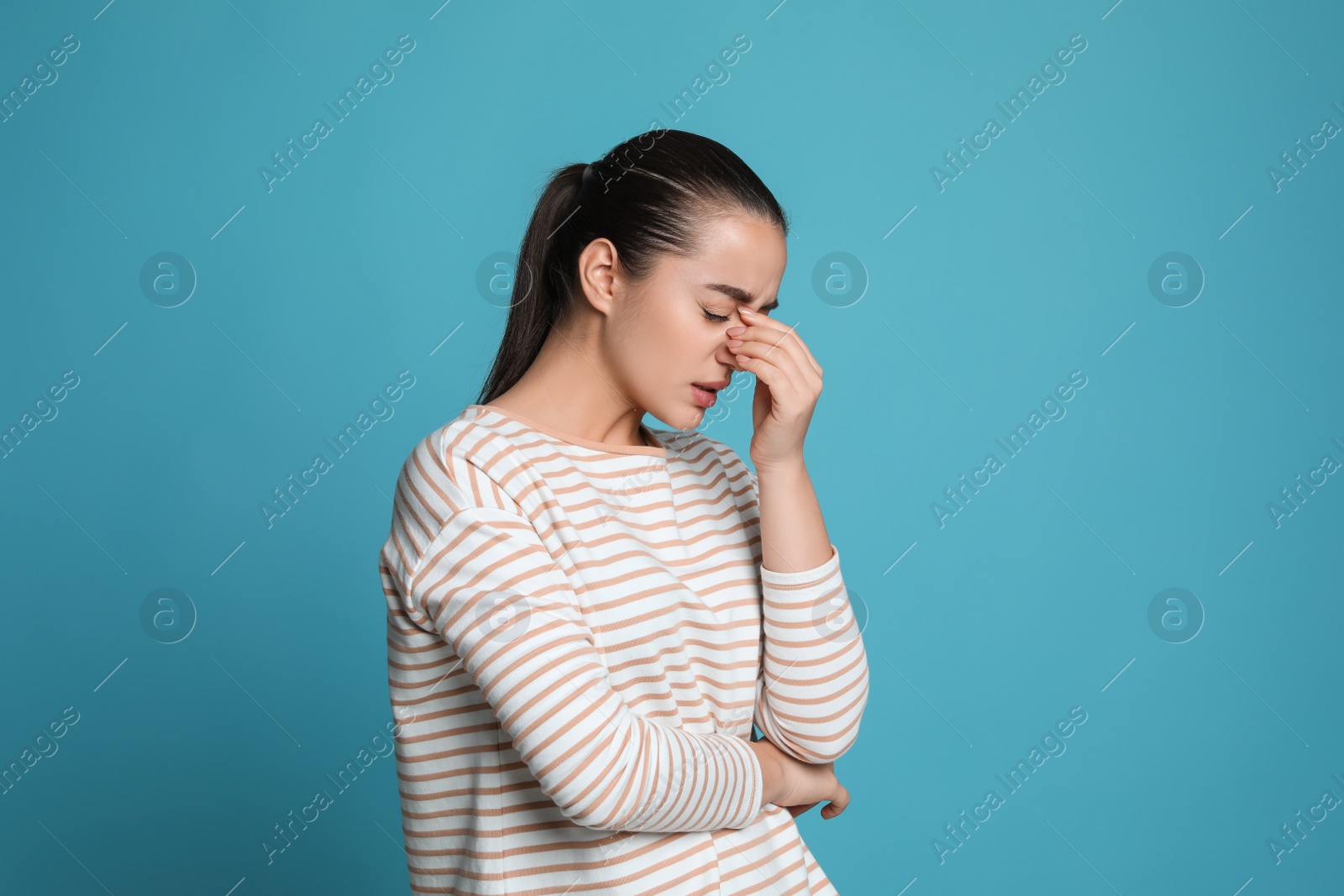 Photo of Young woman suffering from headache on light blue background