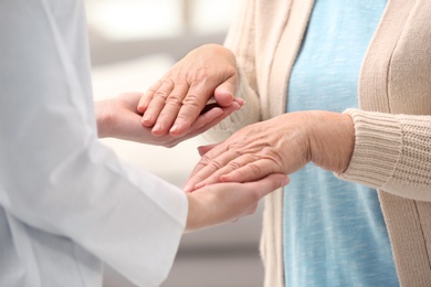 Photo of Nurse comforting elderly woman against blurred background, closeup. Assisting senior generation