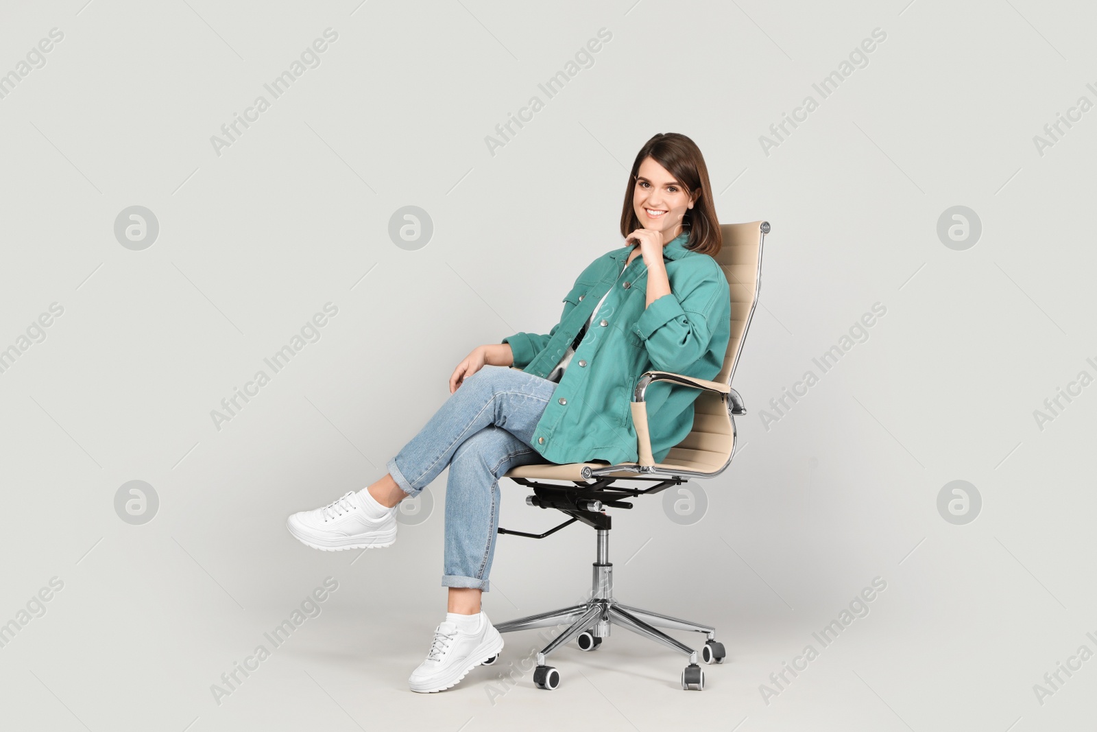 Photo of Young woman sitting in comfortable office chair on grey background