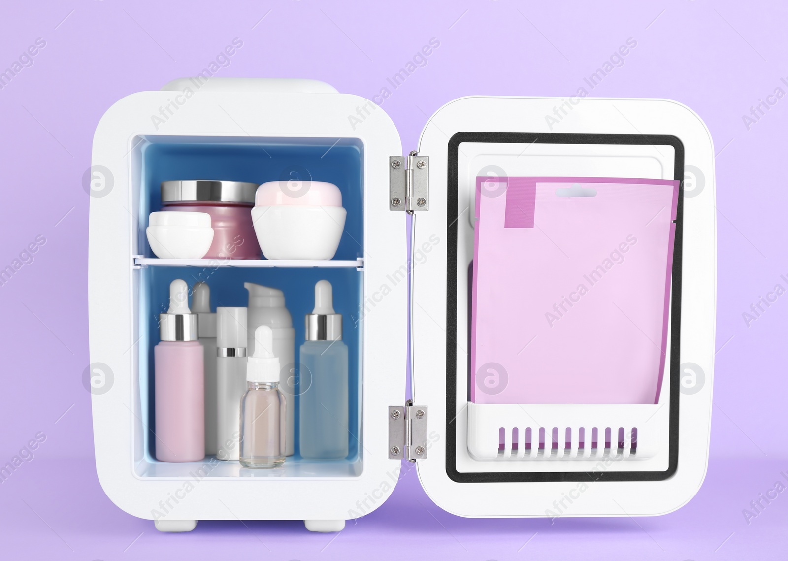 Photo of Open cosmetic refrigerator with skin care products on violet background