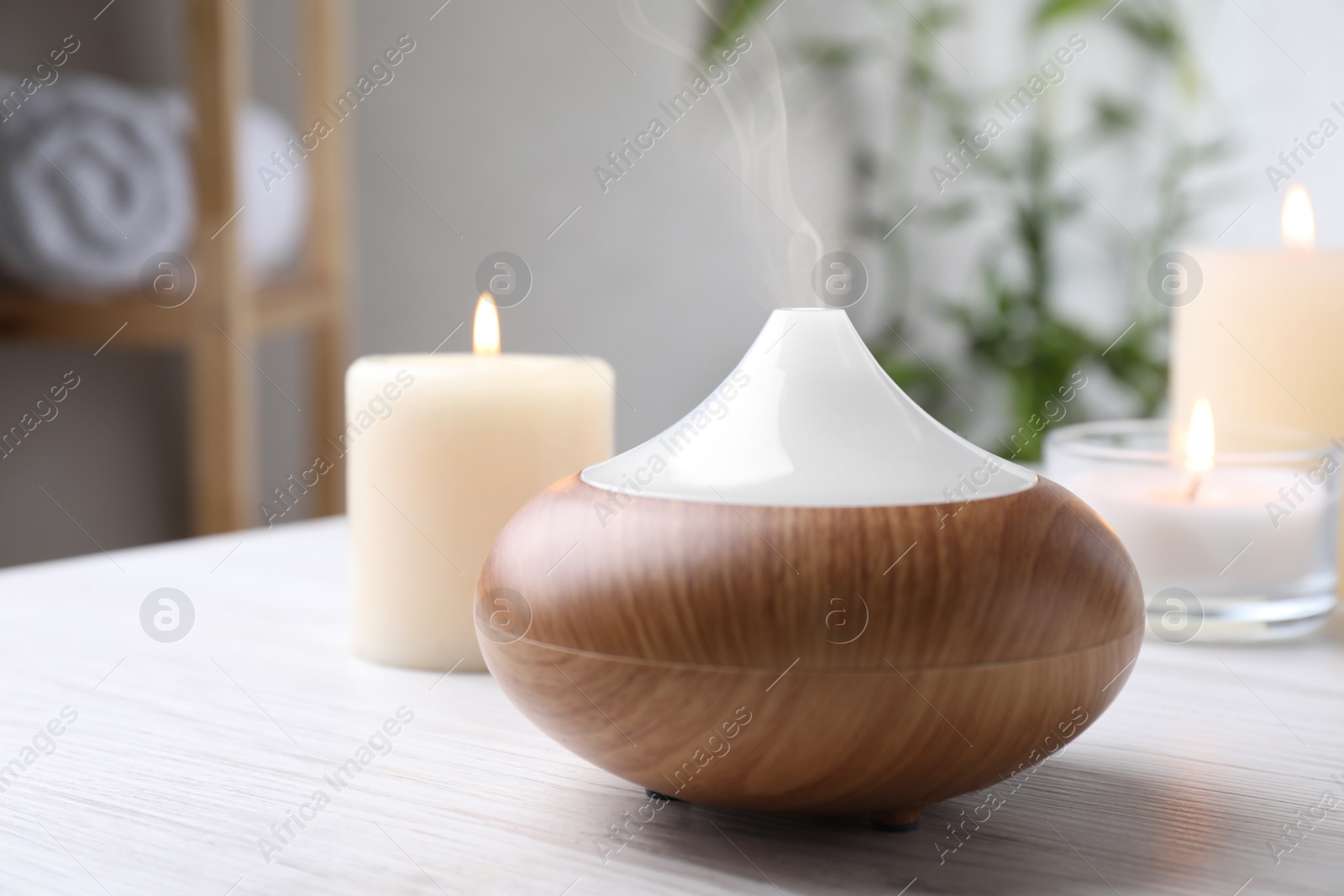 Photo of Aroma oil diffuser and burning candles on white wooden table indoors, space for text