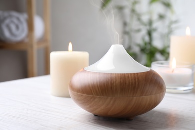 Photo of Aroma oil diffuser and burning candles on white wooden table indoors, space for text