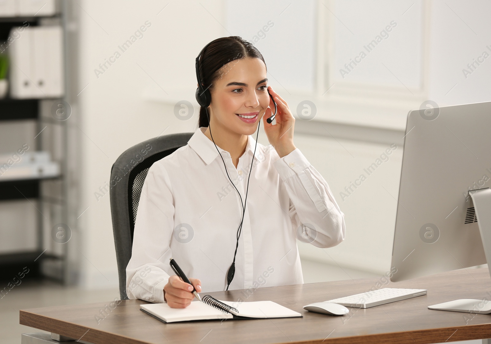 Photo of Hotline operator with headset and notebook working in office