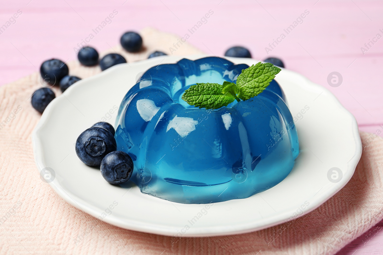 Photo of Plate of delicious blue jelly with berries on pink wooden background