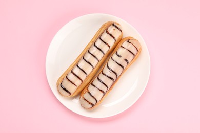 Delicious eclairs covered with glaze on pink background, top view