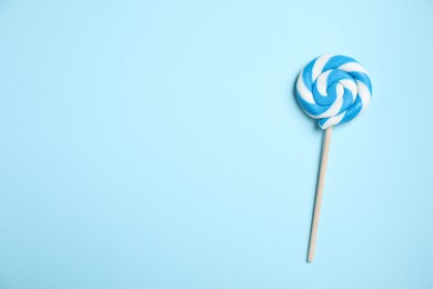 Photo of Stick with bright lollipop on light blue background, top view. Space for text