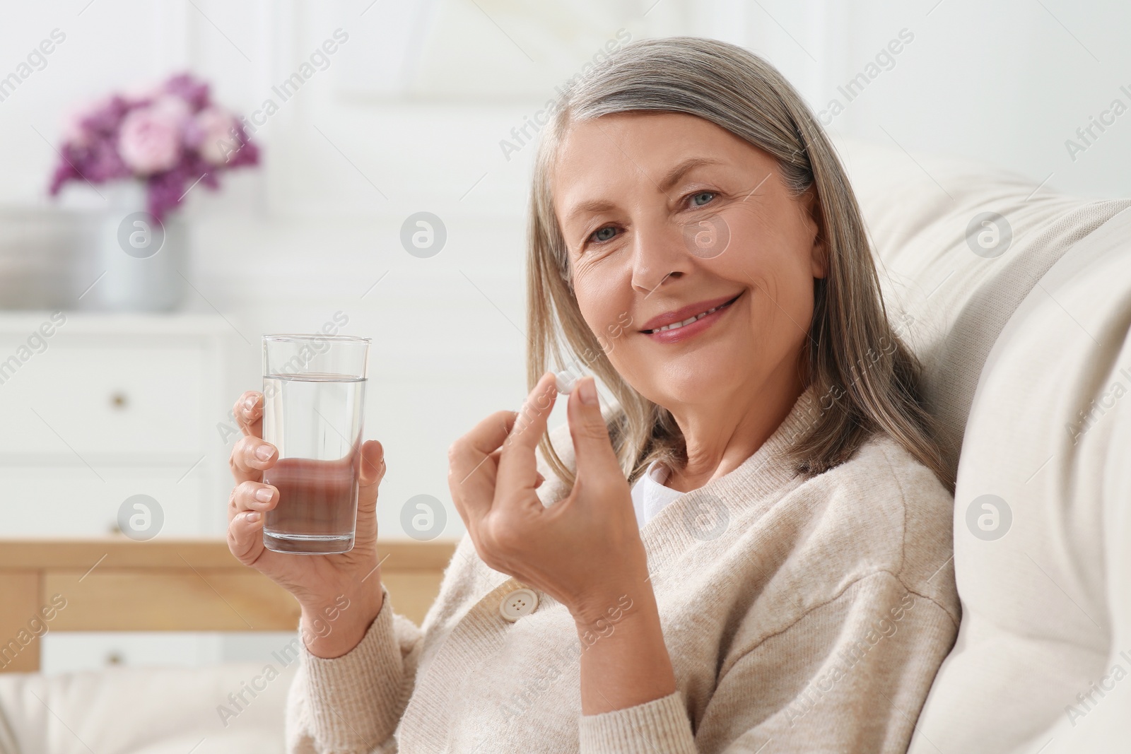 Photo of Senior woman with glass of water taking pill indoors