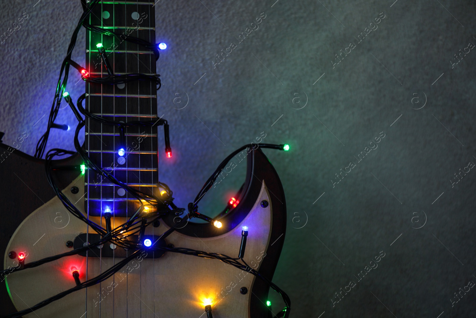 Photo of Guitar with colorful lights on grey stone background, space for text. Christmas music