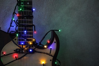 Photo of Guitar with colorful lights on grey stone background, space for text. Christmas music